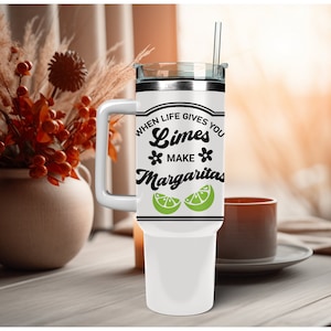 May include: White stainless steel travel mug with a black handle and a black and white graphic that says "When life gives you limes make margaritas" with a lime wedge graphic.