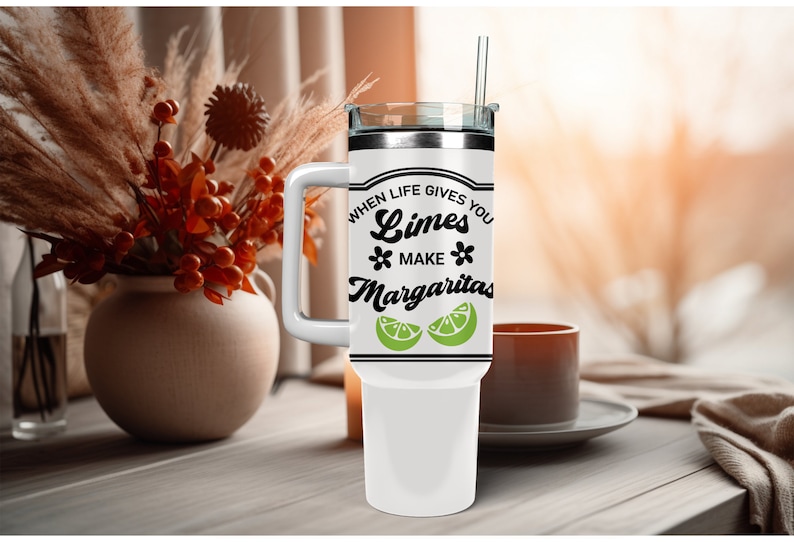 May include: White stainless steel travel mug with a black handle and a black and white graphic that says "When life gives you limes make margaritas" with a lime wedge graphic.