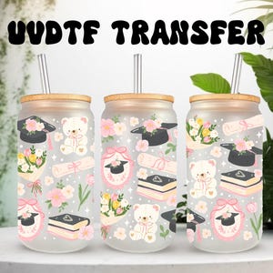 May include: Three glass tumblers with bamboo lids and straws, decorated with graduation-themed graphics. Each tumbler features a teddy bear, graduation cap, diploma, flowers, and books in pink, black, and yellow.