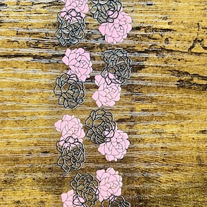 May include: A collection of floral stickers. The stickers feature a design of a rose in pink and black with a black outline. The stickers are arranged in rows on a wooden surface.