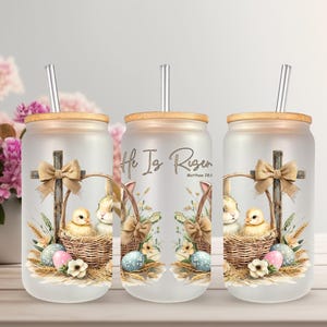 May include: Three frosted glass tumblers with bamboo lids and silver straws. Each tumbler features an Easter-themed design with a cross, a basket with a chick and bunny, and the text "He Is Risen". The design includes pastel eggs and floral accents.