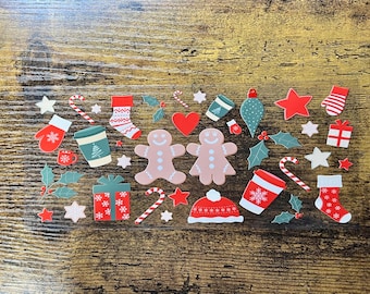 Op de afbeelding: Een transparant stickervel met diverse kerstgerelateerde illustraties, waaronder peperkoekmannetjes, rood-witte zuurstokken, kerstsokken, cadeautjes, hulstblaadjes, sterren, koffiebekers, een rode wintermuts en kerstballen.