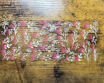 May include: A clear sheet of adhesive decals featuring a variety of botanical illustrations including flowers, leaves, and sprigs. The designs are rendered in a gradient color scheme that transitions from white to vibrant pink, arranged in a pattern.