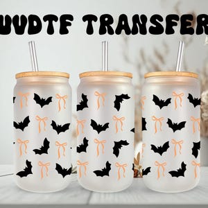 May include: Three frosted glass tumblers with bamboo lids and straws. Each tumbler is decorated with a pattern of black bats and orange bows. The text "UVDTF TRANSFER" is above the tumblers. Halloween-themed drinkware.