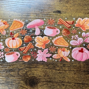 May include: A collection of autumn-themed stickers featuring pumpkins, pie slices, acorns, cinnamon sticks, leaves, mushrooms, and mugs of hot chocolate. The stickers are in shades of orange, pink, and brown.