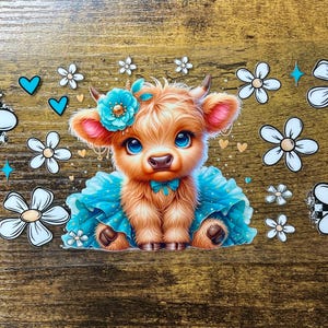 Puede incluir: Ilustración caprichosa de una ternera de vaca de las Tierras Altas con grandes ojos azules, vestida con un vestido azul y una corona de flores. La imagen está decorada con margaritas blancas, corazones azules y estrellas, sobre un fondo de vetas de madera.
