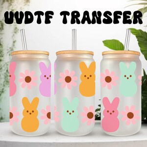 Pode incluir: Três copos de vidro fosco com tampas de bambu e canudos de metal. Cada copo apresenta um design de coelho e flor de cores diferentes. As cores incluem rosa, laranja e verde menta. O texto "UVDTF TRANSFER" está no topo.