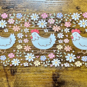 Puede incluir: Un diseño rectangular con tres pollos de dibujos animados de color azul claro con crestas rojas, rodeados de flores coloridas. Las flores incluyen pétalos rosas, amarillos y azules con hojas verdes, creando un patrón alegre y primaveral.