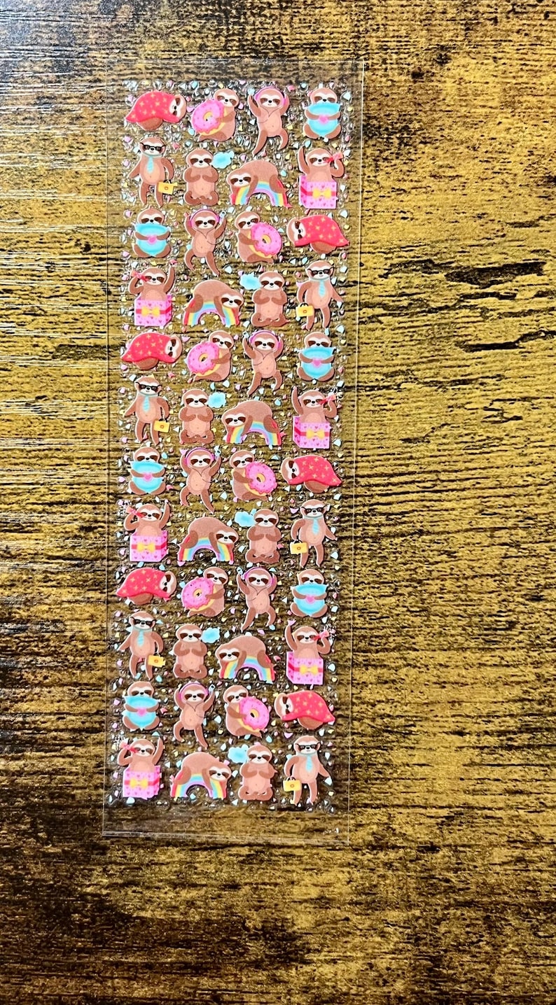 May include: A sheet of stickers featuring various cartoon sloths. The sloths are depicted in different poses, some wearing sunglasses, holding donuts, or carrying briefcases. The stickers have a glittery finish and are in various colors.