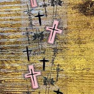 May include: A clear sticker sheet featuring a repeating pattern of pink crosses with black outlines, black crosses, and black floral-adorned crosses. The word Blessed is written in a black cursive script throughout the design.