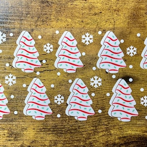 May include: A collection of Christmas tree-shaped decorations with red and green striped details. White snowflakes and dots are scattered around the trees. The decorations are arranged on a wooden surface.