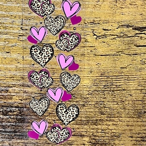 May include: A sheet of heart-shaped stickers. The stickers feature a combination of pink, leopard print, and solid pink hearts. The stickers are arranged in rows and columns on a clear backing, perfect for crafts and decorations.