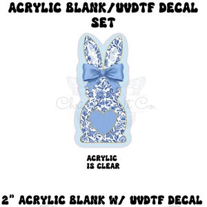 May include: A 2-inch acrylic bunny blank with a UVDTF decal. The bunny has a blue bow and a blue heart. The bunny is decorated with a blue and white floral pattern. The text "ACRYLIC IS CLEAR" is visible.
