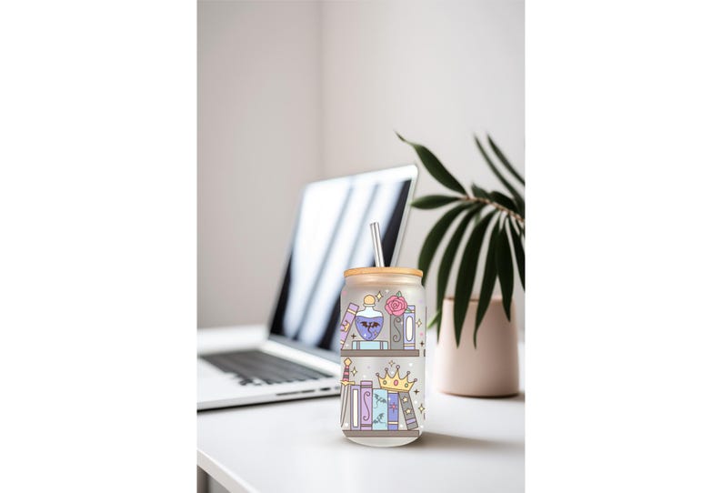 May include: A glass tumbler with a bamboo lid and straw, decorated with a whimsical bookshelf design. The illustration features books, potion bottles, a crown, and a rose in pastel colors. The tumbler is on a white surface with a laptop and plant in the background.