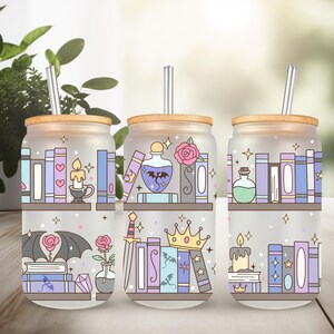 May include: Three frosted glass drink cups with bamboo lids and straws. Each cup features a whimsical design of bookshelves with books, candles, potions, and other fantasy-themed elements in pastel colors. The cups are on a wooden surface.