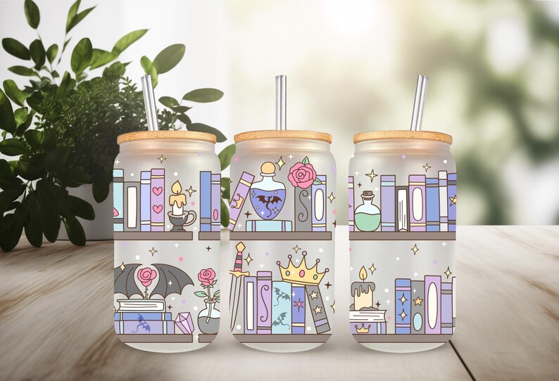 May include: Three frosted glass drink cups with bamboo lids and straws. Each cup features a whimsical design of bookshelves with books, candles, potions, and other fantasy-themed elements in pastel colors. The cups are on a wooden surface.