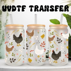 Puede incluir: Tres recipientes de vidrio para bebidas con tapas y pajitas de bambú. Cada recipiente presenta un diseño caprichoso de gallinas, huevos y elementos florales. El texto "UVDTF TRANSFER" está impreso en la parte superior. Los recipientes están sobre una superficie blanca.