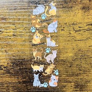 Puede incluir: Hoja de pegatinas transparente con varios gatos de dibujos animados en diferentes poses y colores, incluyendo gris, amarillo y marrón. La palabra "meow" está escrita en cursiva encima y debajo de los gatos, junto con huellas de patas.