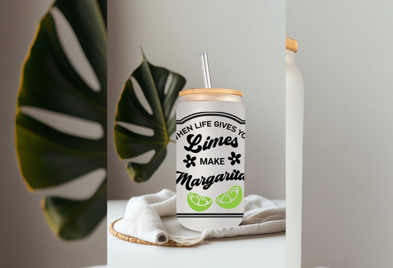 May include: A white frosted glass can with a bamboo lid and a straw. The can has a black graphic that says "When life gives you limes, make margaritas" with two green lime slices.