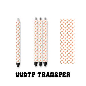 May include: Three white pens with a peach pattern and a sheet of the same pattern. The text "UV DTF TRANSFER" is printed below the pens.