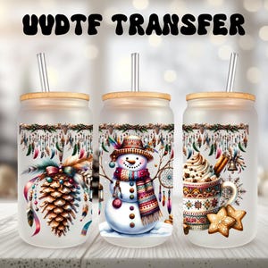 May include: Three frosted glass tumblers with bamboo lids and clear straws. Each tumbler features a different winter-themed design: a pine cone with feathers, a snowman wearing a colourful scarf, and a mug of hot chocolate with a star-shaped cookie.