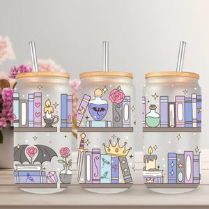 May include: Three glass tumblers with wooden lids and silver straws. Each tumbler features a whimsical design of bookshelves, candles, potions, and other fantasy-themed elements in pastel colors. The tumblers are ideal for cold beverages.