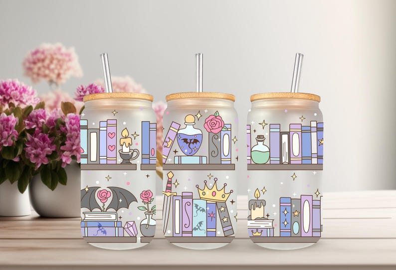 May include: Three glass tumblers with wooden lids and silver straws. Each tumbler features a whimsical design of bookshelves, candles, potions, and other fantasy-themed elements in pastel colors. The tumblers are ideal for cold beverages.