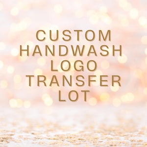 May include: Custom handwash logo transfer lot. The text is in gold against a blurred background of pink and white with gold lights.