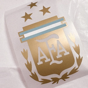 May include: Gold and blue vinyl decal of the Argentine Football Association (AFA) logo. The logo features a shield with the letters "AFA" inside, two horizontal blue stripes, and three gold stars above the shield. The shield is surrounded by a laurel wreath.
