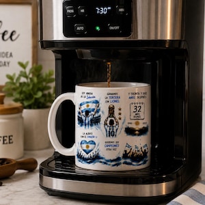 May include: A white ceramic mug featuring a graphic print of a soccer player holding a trophy, the Argentine flag, and text in Spanish including "Soy hincha de la Selecci&oacute;n," "Ganamos la tercera con Lionel," and "Y treinta y dos a&ntilde;os despu&eacute;s."