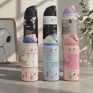 Op de afbeelding: Verschillende ge&iuml;soleerde waterflessen in pastelkleuren, met een cartoon hond ontwerp. Elke fles heeft een deksel en een rietje in een andere kleur. De flessen zijn gestapeld en tonen de merknaam en productkenmerken.
