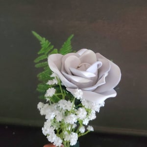 May include: A single white rose with a small cluster of white baby's breath and green foliage.