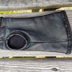 May include: Black leather wrist warmer with a braided edge and a hole in the center.