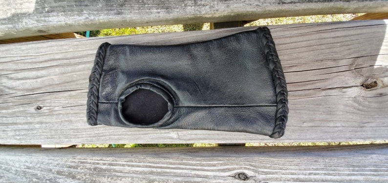 May include: Black leather wrist warmer with a braided edge and a hole in the center.