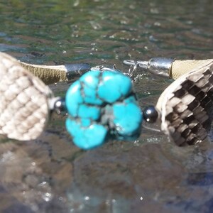 May include: A turquoise gemstone bracelet with a silver clasp and two leather straps. The leather straps are patterned with a scale-like design.
