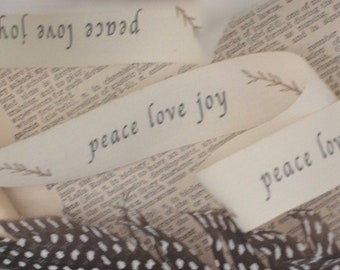 May include: A close-up of a book with white ribbon tied around it. The ribbon has the words "peace love joy" written on it. A black and white feather is lying on top of the book.