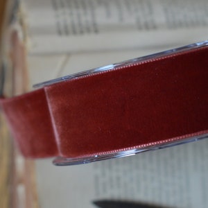 May include: A spool of dark red velvet ribbon on a clear plastic spool. The ribbon is wound around the spool and is ready to be used for crafting or decorating.