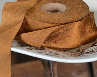 May include: A roll of brown satin ribbon with a frayed edge, sitting on a white porcelain plate with a floral design.