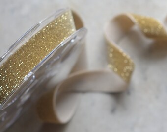 May include: A spool of gold glitter ribbon with a beige velvet ribbon.