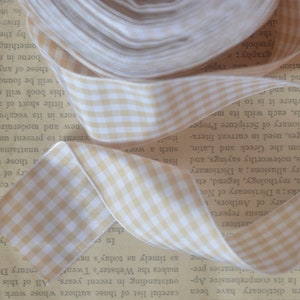 May include: A roll of beige and white gingham ribbon with a white edge. The ribbon is folded and rolled up on a book.