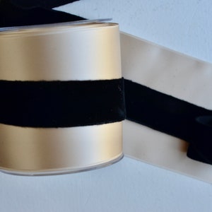 May include: A spool of beige satin ribbon with a black velvet ribbon wrapped around it.