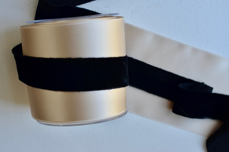 May include: A spool of beige satin ribbon with a black velvet ribbon wrapped around it.