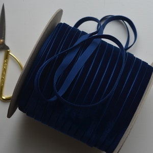 Könnte beinhalten: Eine Spule mit dunkelblauem Samtband, das um einen Kartonkern gewickelt ist. Das Band ist etwa 1,2 cm breit.