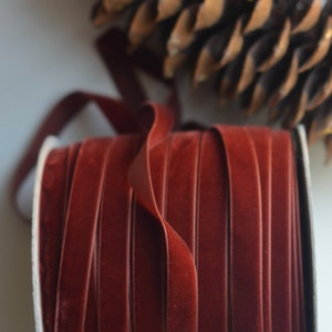 May include: A spool of deep red velvet ribbon. The ribbon is wound tightly around a white cardboard core.