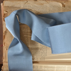 May include: A light blue ribbon is folded and placed on top of an open book. The ribbon is made of a soft, textured fabric.