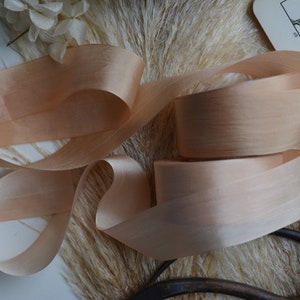 May include: A close-up of a spool of peach-colored satin ribbon. The ribbon is soft and silky, with a subtle sheen. It is perfect for adding a touch of elegance to any project.