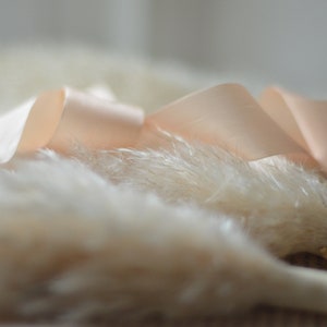 May include: A close-up of a fluffy white pampas grass bouquet tied with a soft peach satin ribbon.