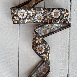 May include: A roll of black and white floral ribbon with brown accents. The ribbon is embroidered with small white flowers and brown leaves.