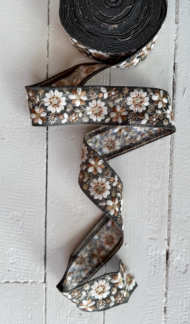 May include: A roll of black and white floral ribbon with brown accents. The ribbon is embroidered with small white flowers and brown leaves.