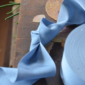 May include: A roll of light blue ribbon with a textured surface. The ribbon is folded into a bow shape and is lying on a wooden surface.